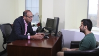 A researcher sitting at his desk speaking with a patient.