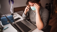 A woman with a mask looking at her computer while on her cell phone