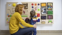 Young mother and her one year old baby son playing with wooden interactive board at psychotherapy office.