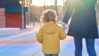 Mother walking hand in hand with her young son enjoying a moment of family togetherness in a park at sunset.