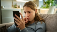 A nervous teen girl looking at her smartphone biting her nails worried about bad news