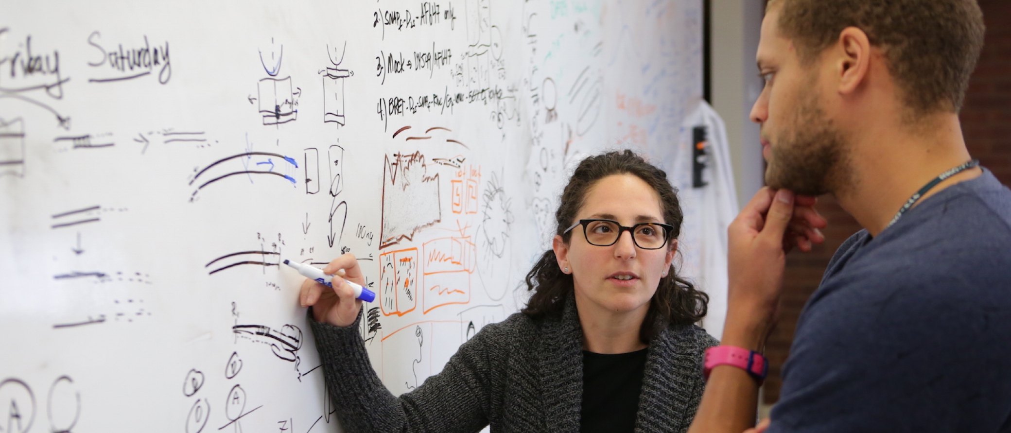 A professor uses a white board to teach a student.